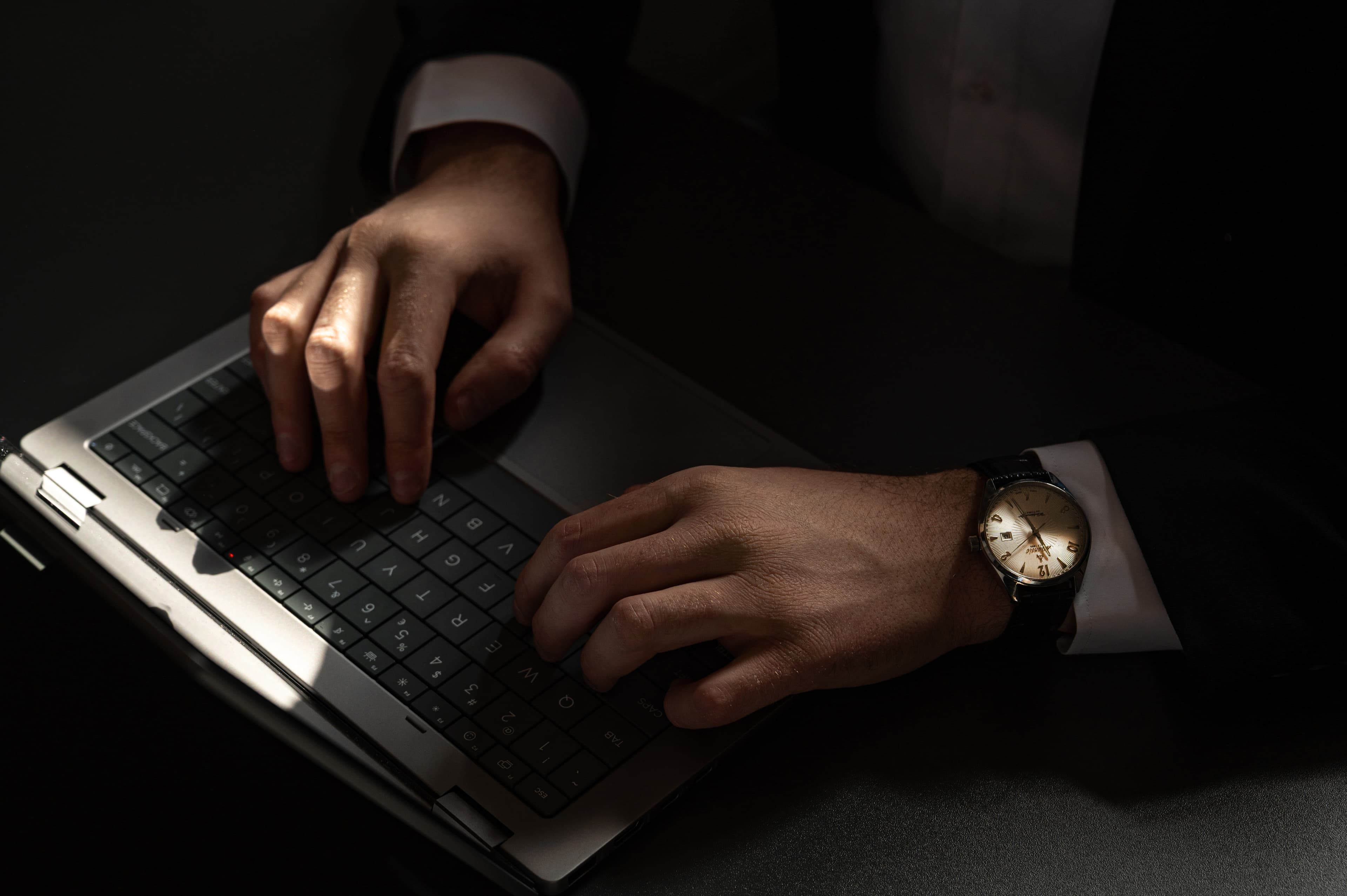 Dłonie mężczyzny w garniturze piszącego na klawiaturze laptopa